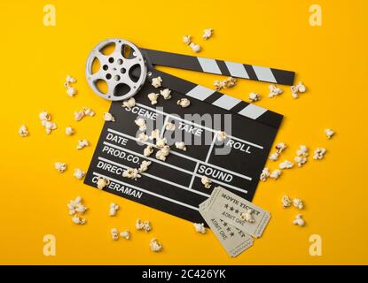 Lit simple, noir, film ouvert clapper ou clapper-board avec bobine de film, pop-corn et billets de cinéma plat Lay Top vue d'en haut sur jaune ou orange Banque D'Images