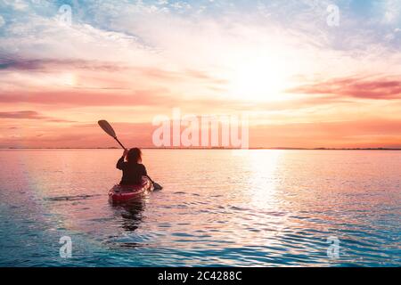 Kayak de mer dans des eaux calmes pendant un coucher de soleil coloré et vibrant. Banque D'Images