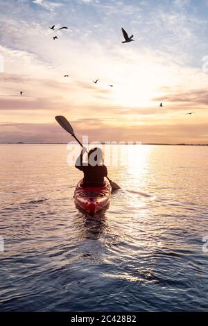 Kayak de mer dans des eaux calmes pendant un coucher de soleil coloré et vibrant. Banque D'Images