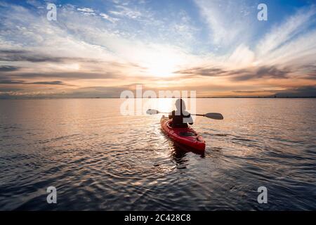 Kayak de mer dans des eaux calmes pendant un coucher de soleil coloré et vibrant. Banque D'Images