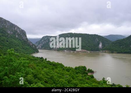 Danube george dans une journée nuageux avec forêt verte en premier plan et falaises, pont, route et statue de Decebalus en arrière-plan Banque D'Images