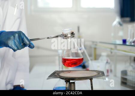 Un technicien de laboratoire chauffe le liquide rouge dans un flacon Erlenmeyer au-dessus d'un brûleur Bunsen Banque D'Images