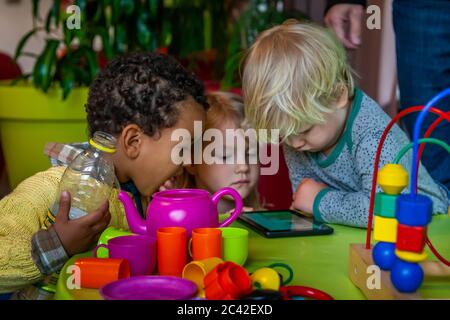 Dans un espace de jeu, trois petits enfants se concentrent sur un smartphone Banque D'Images