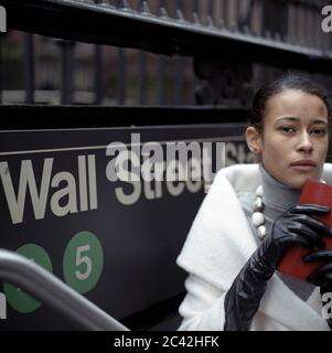 Une femme à la peau sombre monte les escaliers d'une station de métro et tient son portefeuille devant son menton - Wall Street - Business Banque D'Images