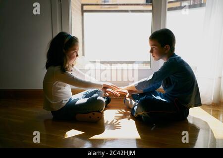deux enfants assis sur le sol jouant avec leurs mains dans l'ombre Banque D'Images