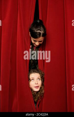 Deux jeunes femmes regardent à travers un rideau rouge Banque D'Images