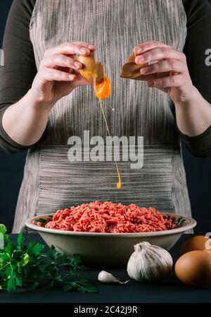 Une femme chef jette un œuf pour aromatiser le bœuf haché et faire cuire des boulettes de viande maison et nutritives. Banque D'Images