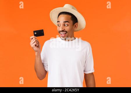 Cheerful, excité smiling african-american bel homme avec chapeau, tee-shirt blanc, à la carte de crédit et souriant heureux, à l'aide de dépôt, payer avec Banque D'Images