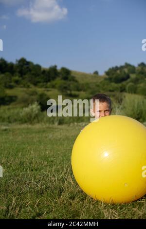 Le petit garçon se cache derrière une grosse balle de caoutchouc - loisir - nature Banque D'Images