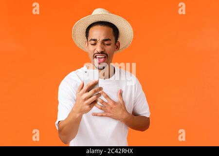 Passionné et excité africain-américain jeune homme, en parlant avec ami en ligne, tenant smartphone, craignant ses meilleures vacances, contact mate pendant Banque D'Images