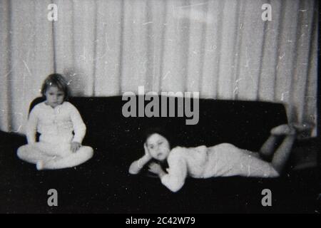 Belle photographie en noir et blanc des années 1970 de deux filles qui traînaient à la maison tout en regardant la télévision. Banque D'Images