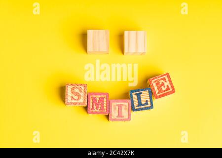 blocs en bois formant un visage souriant sur fond jaune avec espace de copie pour le texte Banque D'Images