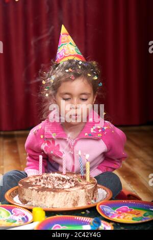 Une petite fille avec un chapeau pointu souffle les bougies d'un gâteau d'anniversaire - fête - enfance Banque D'Images