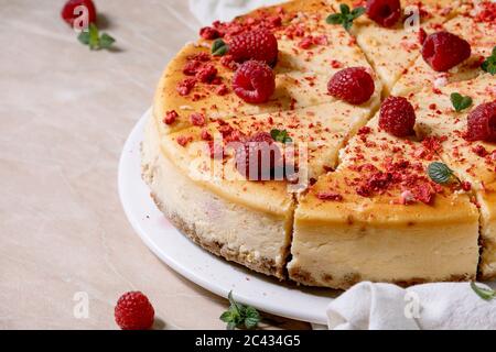 Gâteau au fromage maison, cuit à la framboise, tranché sur une assiette, décoré de framboises fraîches et de menthe sur fond de marbre rose et de tissu blanc. Gros plan Banque D'Images