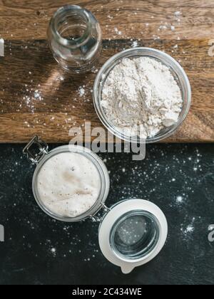 Démarreur de levain de blé. Vue de dessus du bol en verre avec entrée de levain, bouteille d'eau et farine de blé Banque D'Images