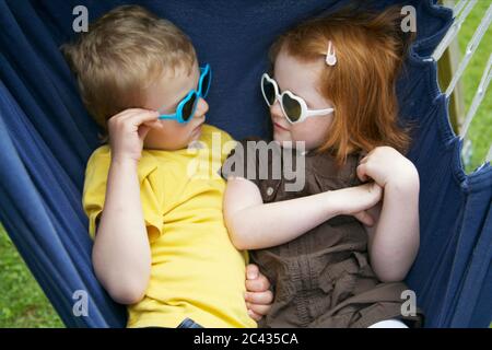 Garçon et fille avec des lunettes de soleil dans une chaise suspendue, Huglfing, Bavière, Allemagne Banque D'Images