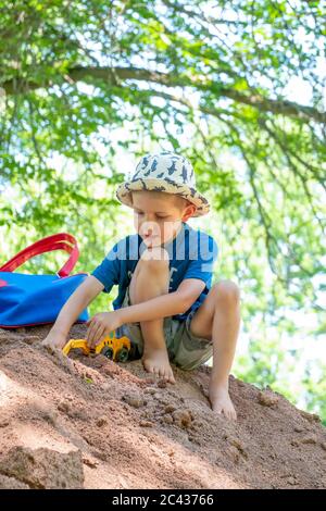 Un jeune enfant joue avec un véhicule de construction sur une grande pile de sable par une journée ensoleillée d'été. Banque D'Images