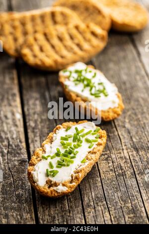 Pain croustillant au fromage crémeux et ciboulette verte sur une table en bois. Banque D'Images