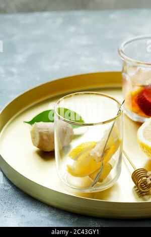 Plateau doré rond avec limonade fraîche maison ou cocktail de gingembre naturel et de fruits au citron dans des verres sur une table grise, espace copie. Froid Banque D'Images