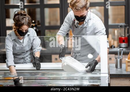 Deux vendeurs de masques et de gants travaillant dans la boutique de crème glacée ou le café. Concept de nouvelles règles pour les entreprises en cas de pandémie Banque D'Images