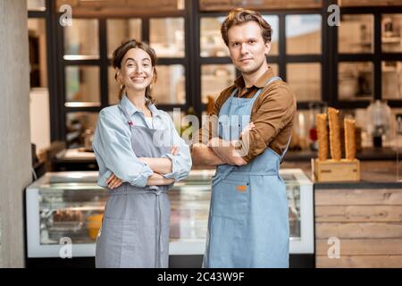 Portrait de deux employés gais d'un café ou d'une petite boutique se tenant devant le comptoir à l'intérieur Banque D'Images