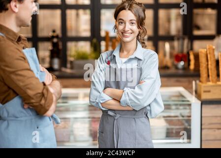 Portrait de deux employés gais d'un café ou d'une petite boutique se tenant devant le comptoir à l'intérieur Banque D'Images