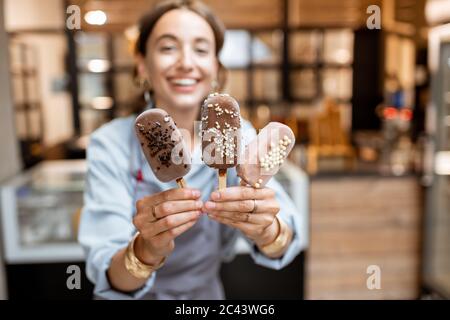 Portrait d'une femme joyeuse vendeur avec glace au chocolat sur un bâton dans la boutique Banque D'Images