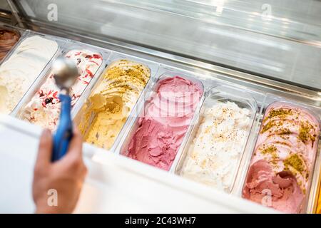 Le vendeur cueillia de la crème glacée avec une cuillère du réfrigérateur dans le magasin. Vue d'en haut sur un plateau rempli de crème glacée aux saveurs différentes Banque D'Images