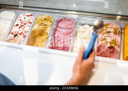 Le vendeur cueillia de la crème glacée avec une cuillère du réfrigérateur dans le magasin. Vue d'en haut sur un plateau rempli de crème glacée aux saveurs différentes Banque D'Images