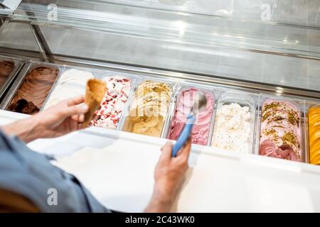 Le vendeur cueillia de la crème glacée avec une cuillère du réfrigérateur dans le magasin. Vue d'en haut sur un plateau rempli de crème glacée aux saveurs différentes Banque D'Images