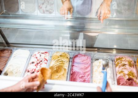 Le vendeur cueillia de la crème glacée avec une cuillère du réfrigérateur dans le magasin. Vue d'en haut sur un plateau rempli de crème glacée aux saveurs différentes Banque D'Images