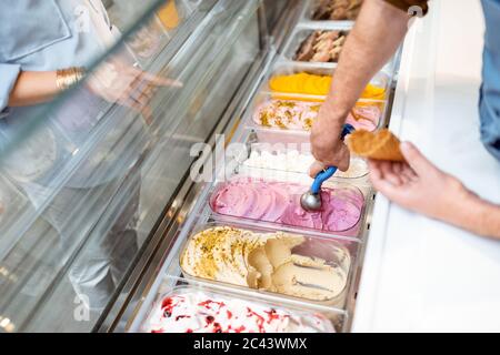 Le vendeur cueillia de la crème glacée avec une cuillère du réfrigérateur dans le magasin. Vue d'en haut sur un plateau rempli de crème glacée aux saveurs différentes Banque D'Images