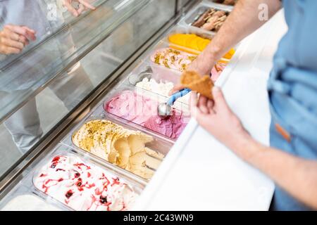 Le vendeur cueillia de la crème glacée avec une cuillère du réfrigérateur dans le magasin. Vue d'en haut sur un plateau rempli de crème glacée aux saveurs différentes Banque D'Images