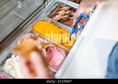 Le vendeur cueillia de la crème glacée avec une cuillère du réfrigérateur dans le magasin. Vue d'en haut sur un plateau rempli de crème glacée aux saveurs différentes Banque D'Images