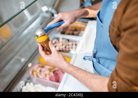 Le vendeur cueillia de la crème glacée avec une cuillère du réfrigérateur dans le magasin. Vue d'en haut sur un plateau rempli de crème glacée aux saveurs différentes Banque D'Images