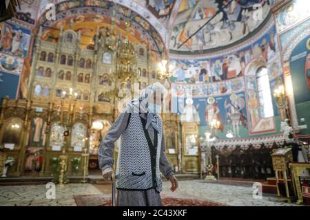 Snagov, Roumanie - 21 juin 2020 : une femme âgée portant un masque Covid-19 prie à l'extérieur d'une église chrétienne orthodoxe. Banque D'Images