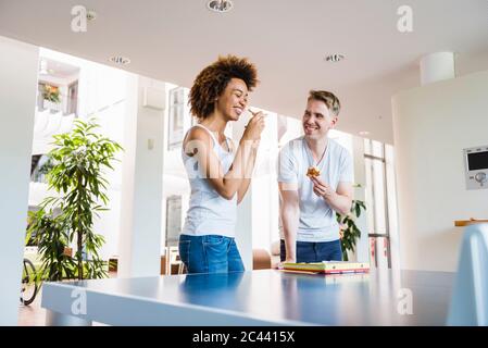 Les jeunes gens d'affaires partagent une pizza pour le déjeuner dans un bureau moderne avec table de ping-pong Banque D'Images