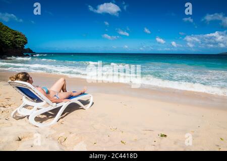 Woman relaxing on lounge chair at beach against blue sky, Grande Anse, Grenade, Caraïbes Banque D'Images