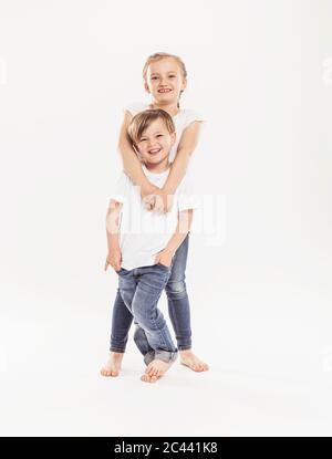 Portrait de la fille souriante et de son frère cadet debout devant un fond blanc Banque D'Images