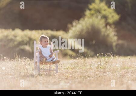 Une petite fille adorable assise sur une chaise dans un pré par beau temps Banque D'Images