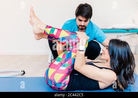 Thérapeute physique masculine malvoyante aidant la femme à faire de l'exercice à la clinique Banque D'Images