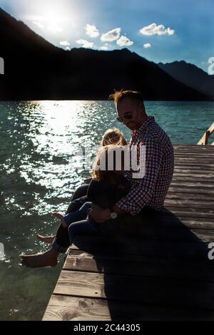Père assis avec des enfants sur la promenade au bord du lac à Achensee, Tyrol, Autriche Banque D'Images