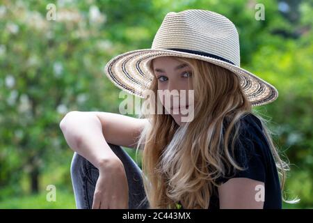 Gros plan d'une fille portant un chapeau assis contre des arbres dans le parc