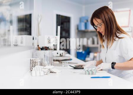 Femme en pleine maturité, sûre d'elle, avec des pilules et une calculatrice à son bureau en laboratoire Banque D'Images