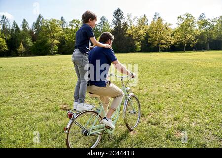 Père et fils profitant de la balade à vélo sur l'herbe pendant la journée ensoleillée Banque D'Images