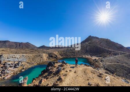 Nouvelle Zélande, île du Nord, soleil qui brille plus de Randonneur admirant des eaux vert émeraude en Parc National de Tongariro Banque D'Images