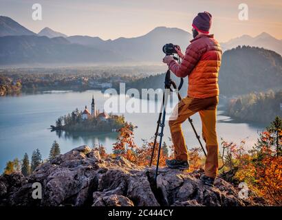 Slovénie, haute-Carniola, Bled, Homme photographiant l'île Bled et Eglise de pèlerinage de l'Assomption de Maria à l'aube brumeuse Banque D'Images