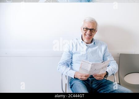 Homme âgé assis dans la salle d'attente de la pratique médicale, lisant la brochure Banque D'Images