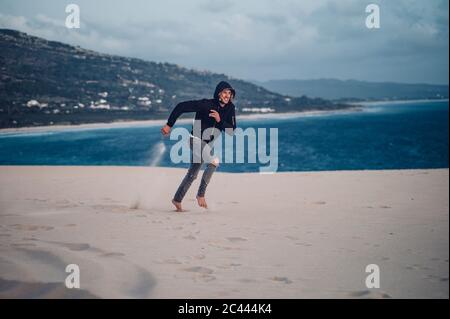 Pleine longueur d'homme courant à la plage contre le ciel à Tarifa, Espagne Banque D'Images