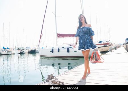 Jeune femme portant une robe marchant sur la jetée contre le ciel clair pendant la journée ensoleillée Banque D'Images